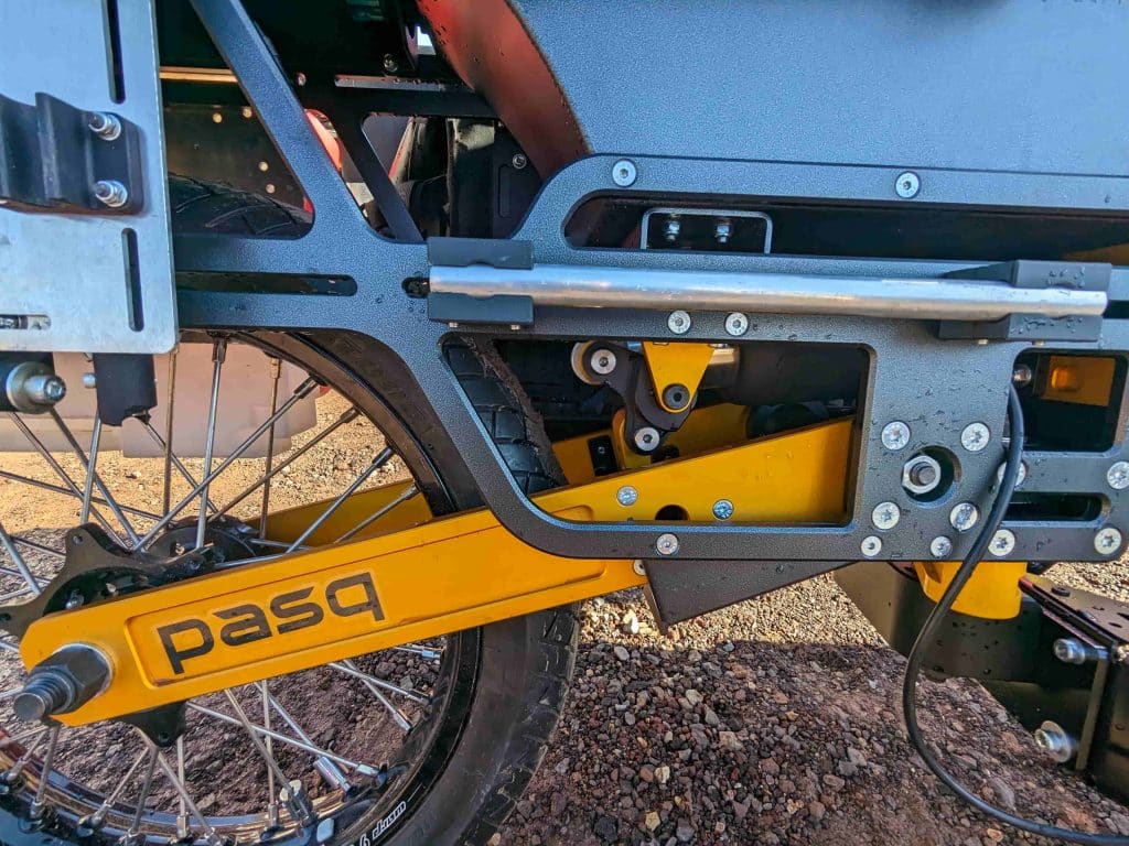 close up of the golden-yelow metal arm connecting the tire to the advi trailer, with the pasq logo on it in black.